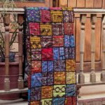 A mosaic Ralli Quilt hanging from a wooden railing
