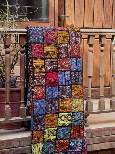 A mosaic Ralli Quilt hanging from a wooden railing