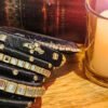 A stack of handcrafted black velvet bangles adorned with gold motifs and crystal accents, displayed on a polished wooden surface beside a flickering candle. The intricate designs reflect the artistry of South Asian craftsmanship.